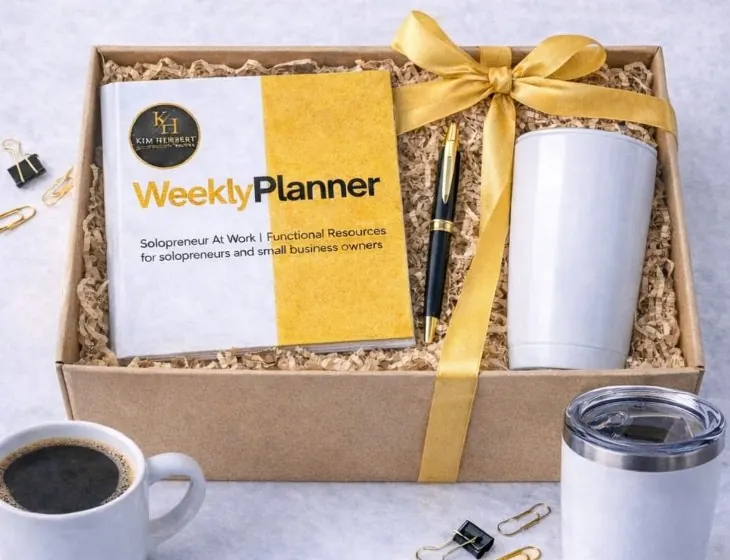 Gift package: the Kim Herbert Weekly Planner, a black and gold pen, and a white tumbler in a kraft box tied with a gold ribbon